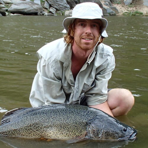 Jerom Stocks crouches in a river, holding a Murray cod.